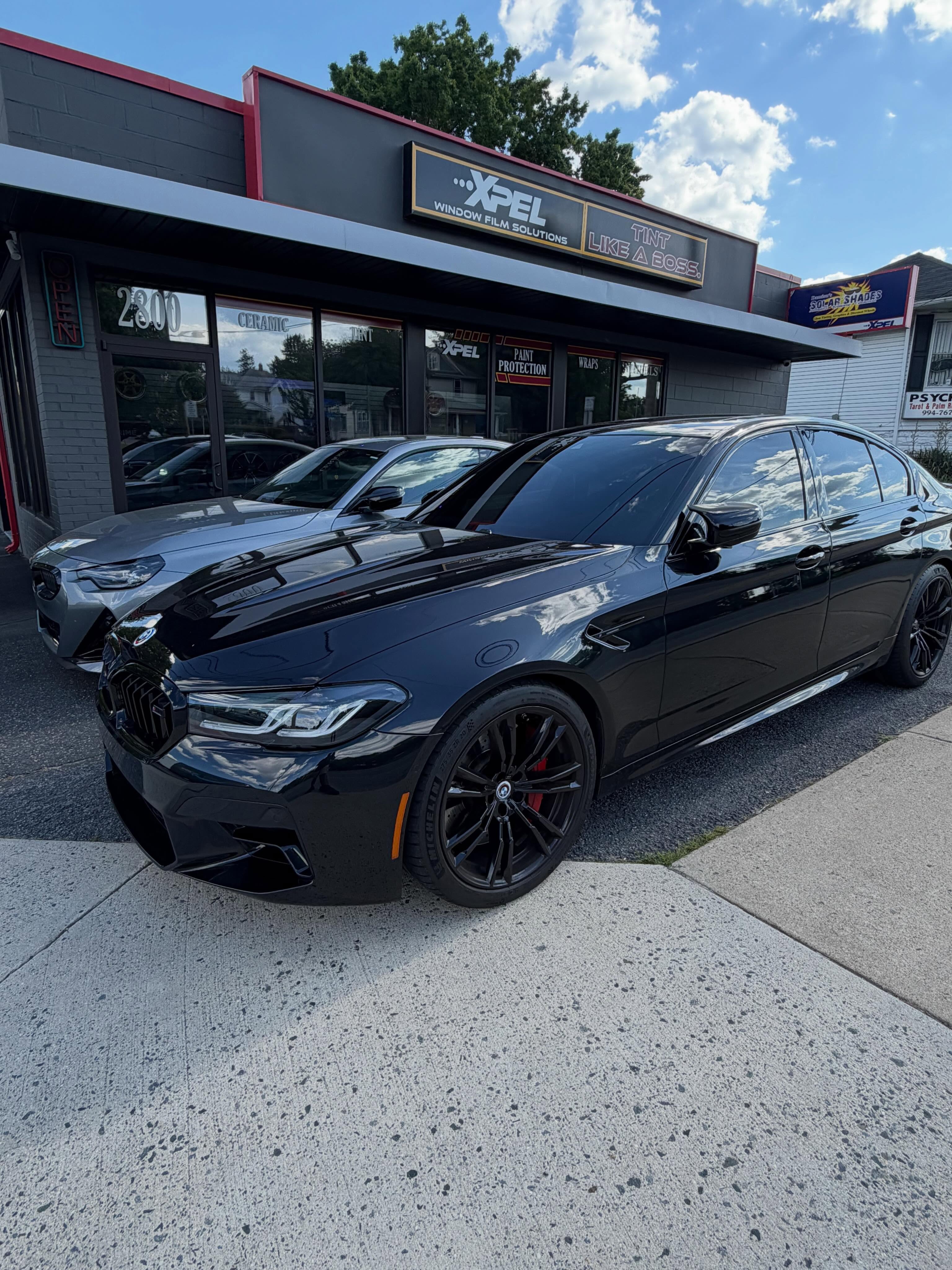 Black BMW sedan with tinted windows in front of the shop's XPEL Window Film Solutions storefront